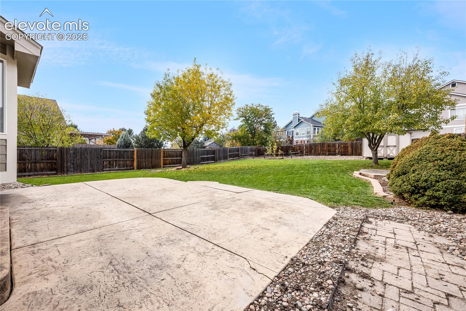 Backyard featuring a concrete patio, lawn, perimeter wood fencing, and a detached storage structure