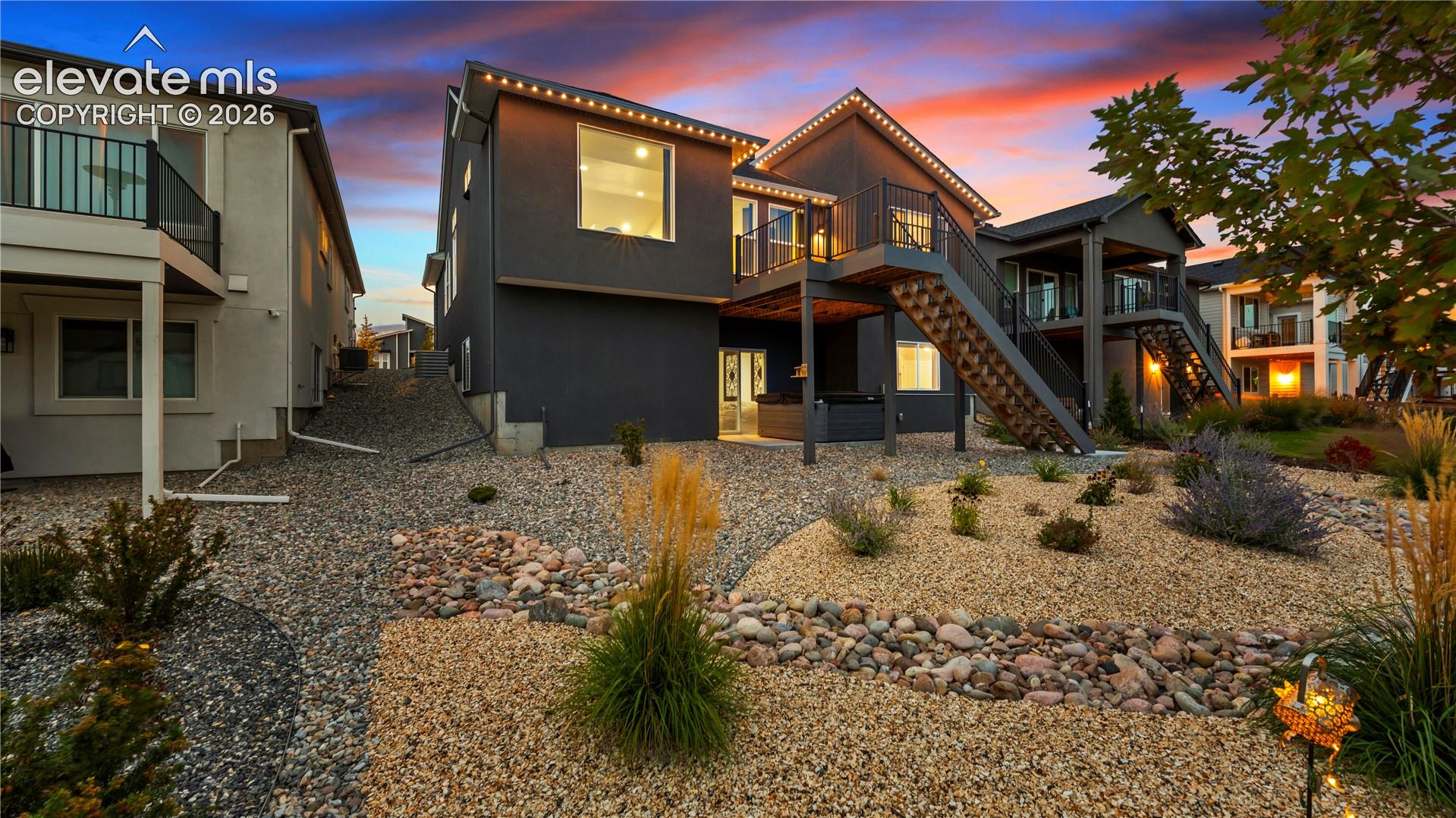 Multi-level residence featuring a dark-toned exterior, raised deck with metal railing, exterior staircase, and low-maintenance xeriscaped lot with stone ground cover