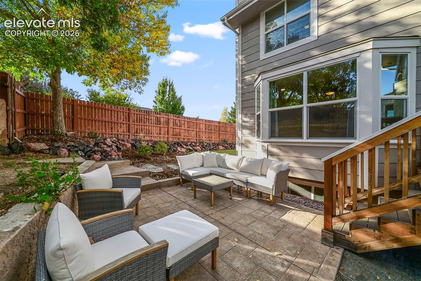 Stoned-pattern patio with a retaining wall, accented by a wood fence and mature trees