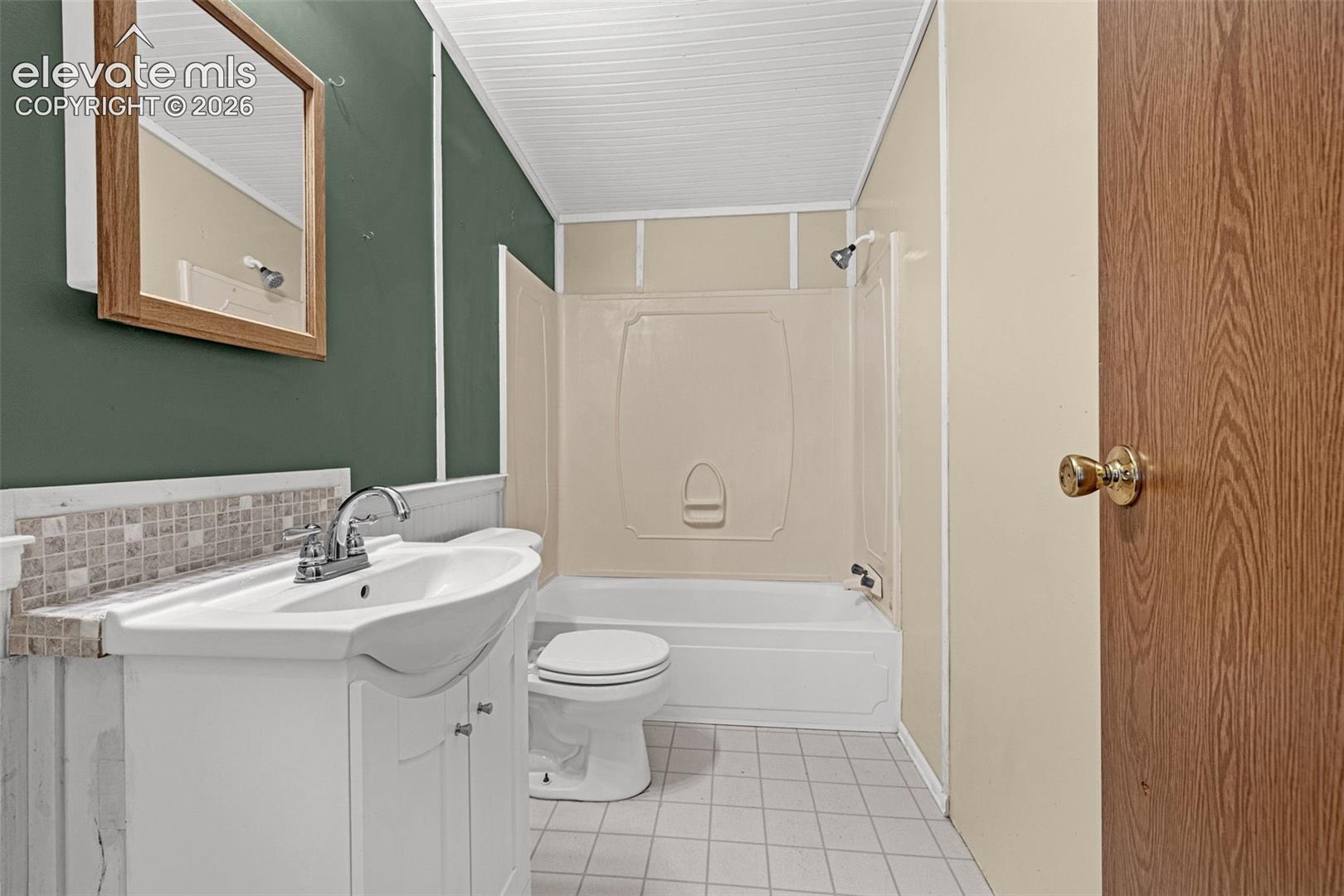 White vanity with an integrated sink, mosaic tile backsplash, and a shower-over-tub combination with a showerhead