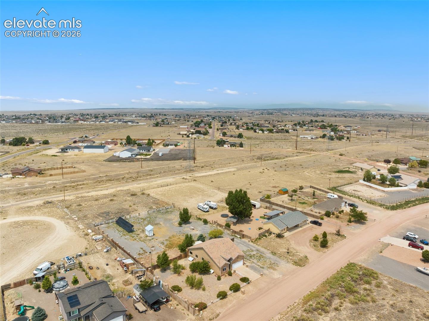 Aerial perspective of a detached residential property featuring a pitched roof, attached garage, and expansive lot with gravel landscaping