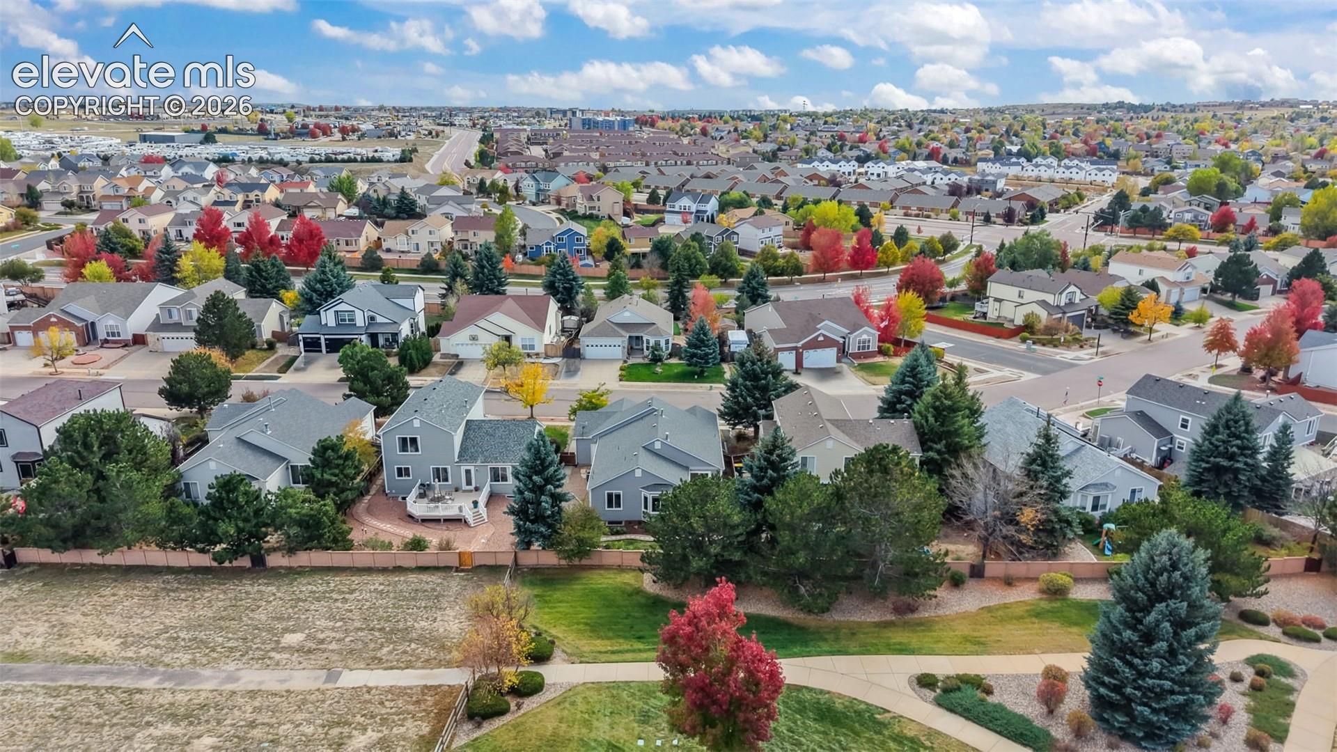 Aerial perspective of a suburban neighborhood featuring a grid of residential properties, paved streets, mature evergreen and deciduous trees, and landscaped common areas