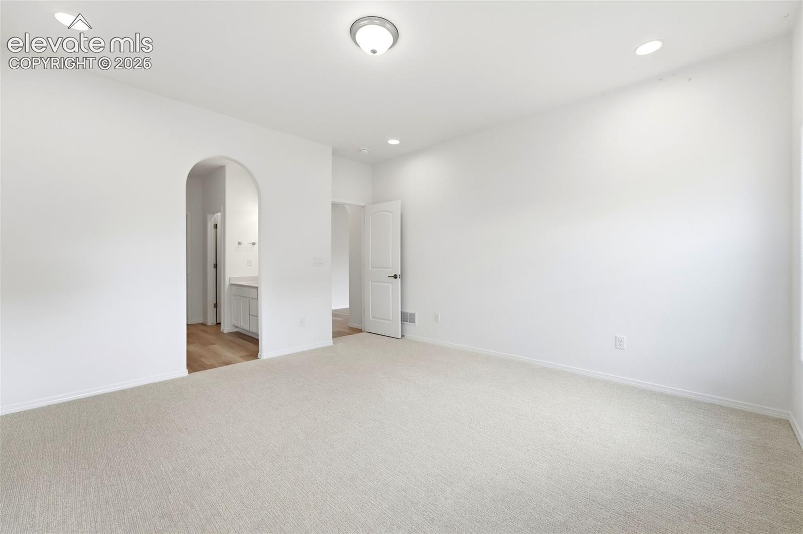 Neutral interior space featuring recessed lighting, carpeting, a paneled door, and an arched entry