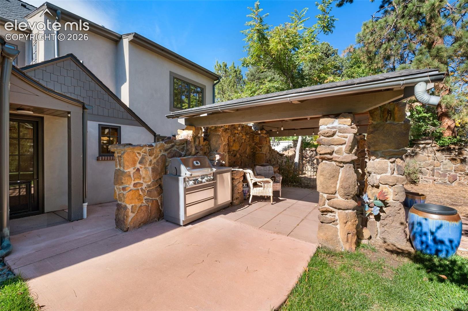 Covered outdoor kitchen featuring natural stone pillars, stone privacy walls, a concrete patio, and a built-in stainless steel grill