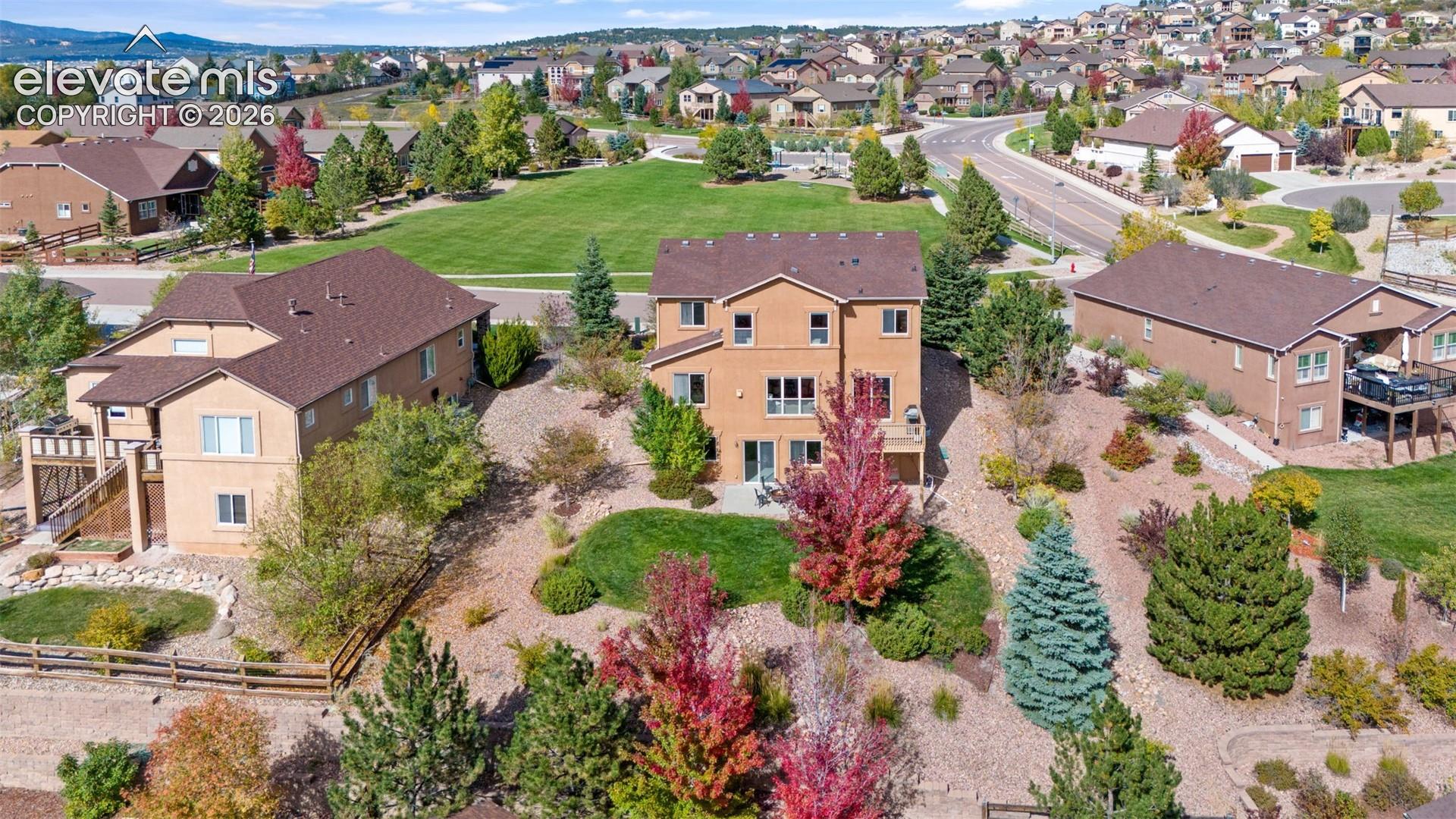 Multi-level residence featuring stucco exterior, shingled roof, elevated deck, concrete patio, and landscaped grounds with mature trees