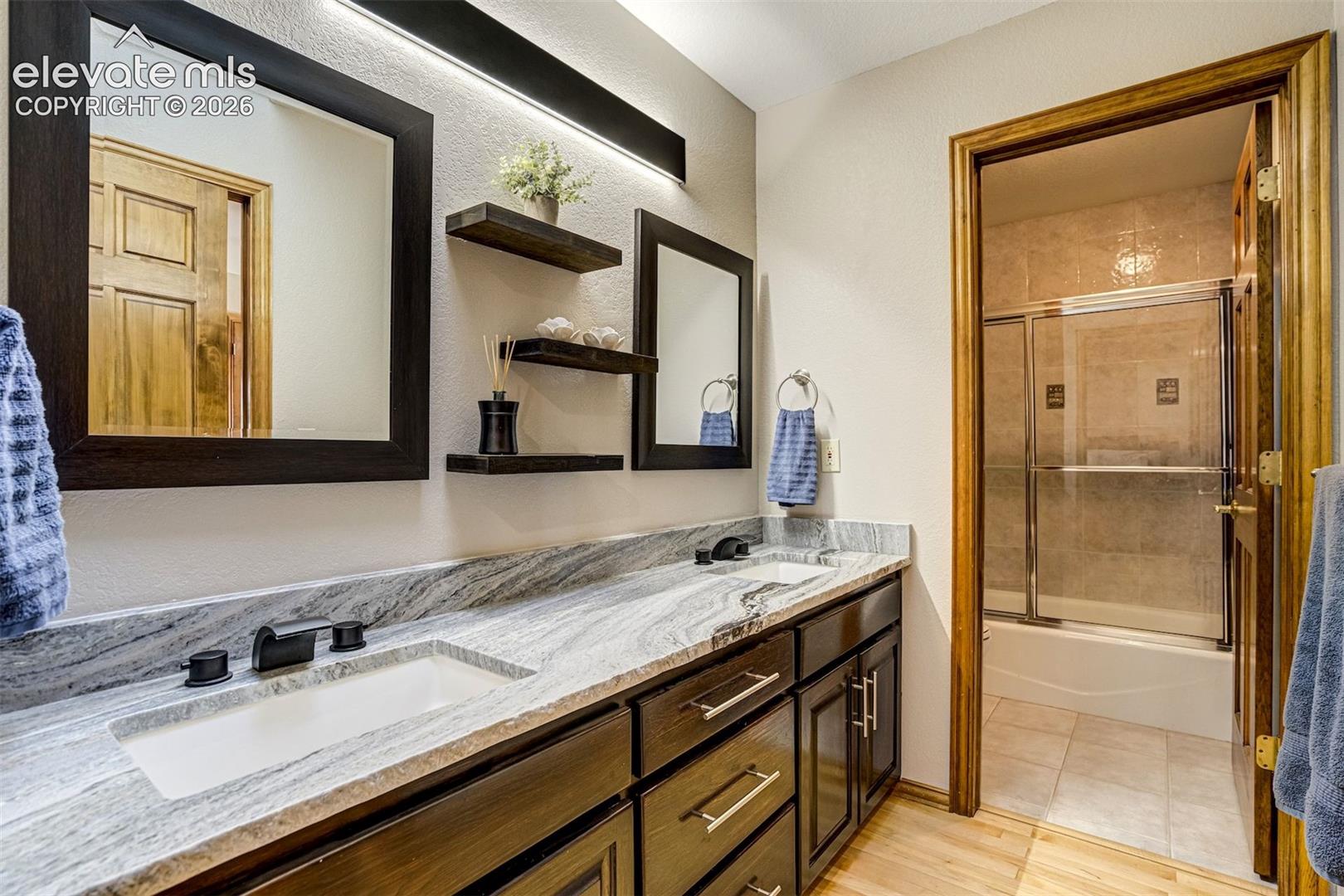 Dual vanity with integrated sinks, patterned stone countertop, dark wood-finish cabinetry, and framed mirrors in Jack and Jill bathroom between 2 secondary bedrooms