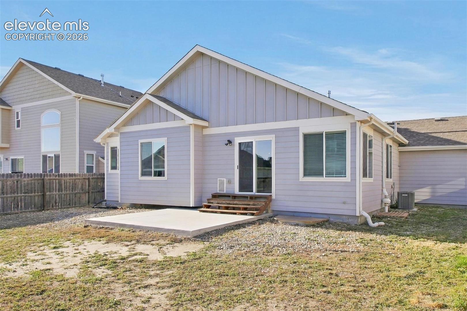 Rear exterior featuring light-toned horizontal siding, vertical board-and-batten gable accents, a concrete patio, and sliding glass doors with wooden step access