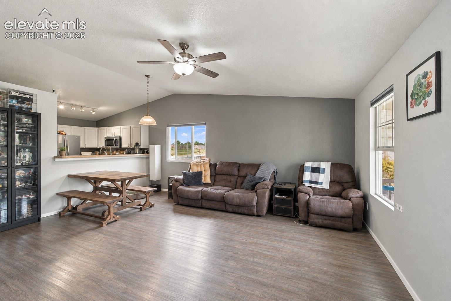 Spacious living area featuring vaulted ceilings, wood-finish flooring, and ample natural light from multiple windows