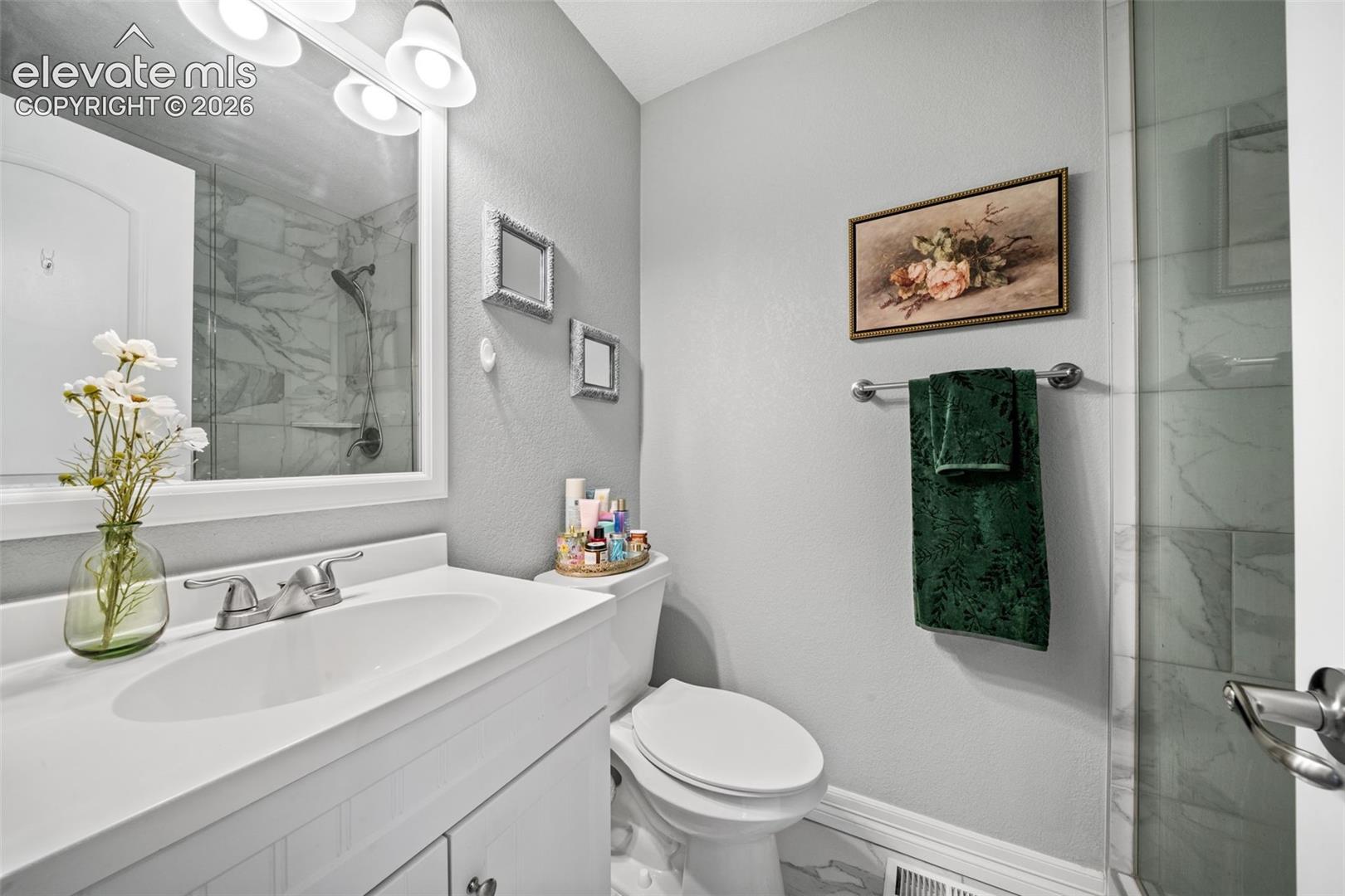 Bathroom featuring a white vanity with integrated sink, chrome faucet, wall-mounted mirror, and a glass-enclosed shower with marble-look tile