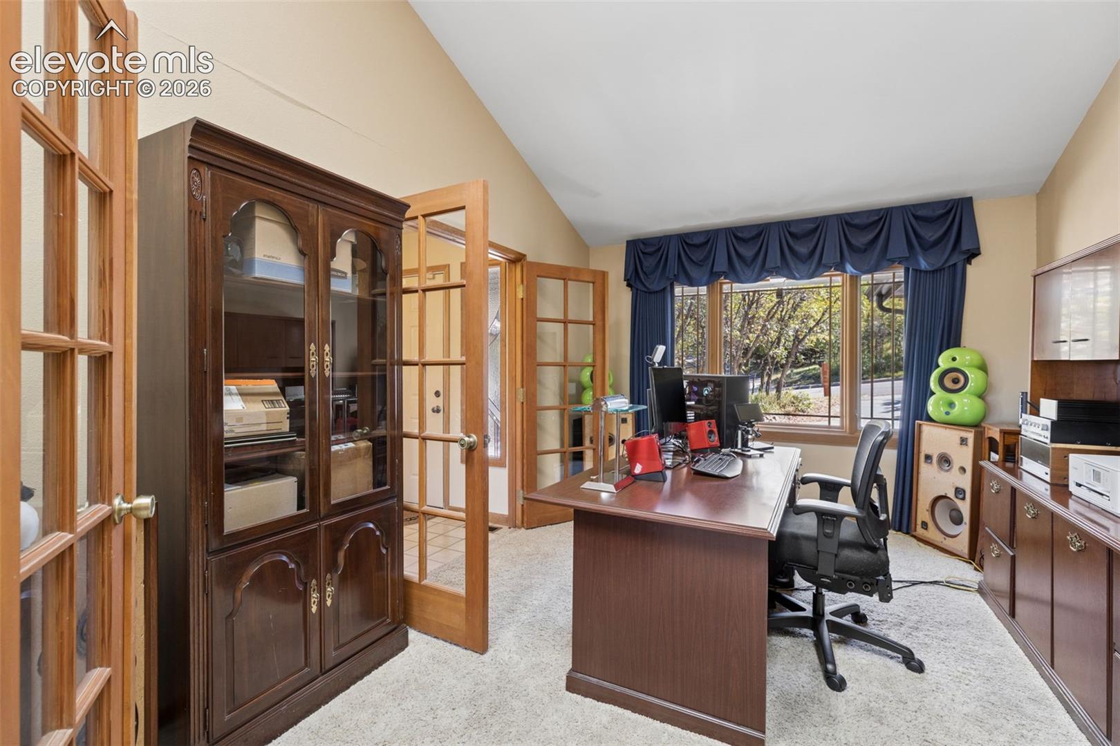 Vaulted ceiling room featuring wood-framed glass-paneled double doors, large multi-pane windows, and built-in wood cabinetry