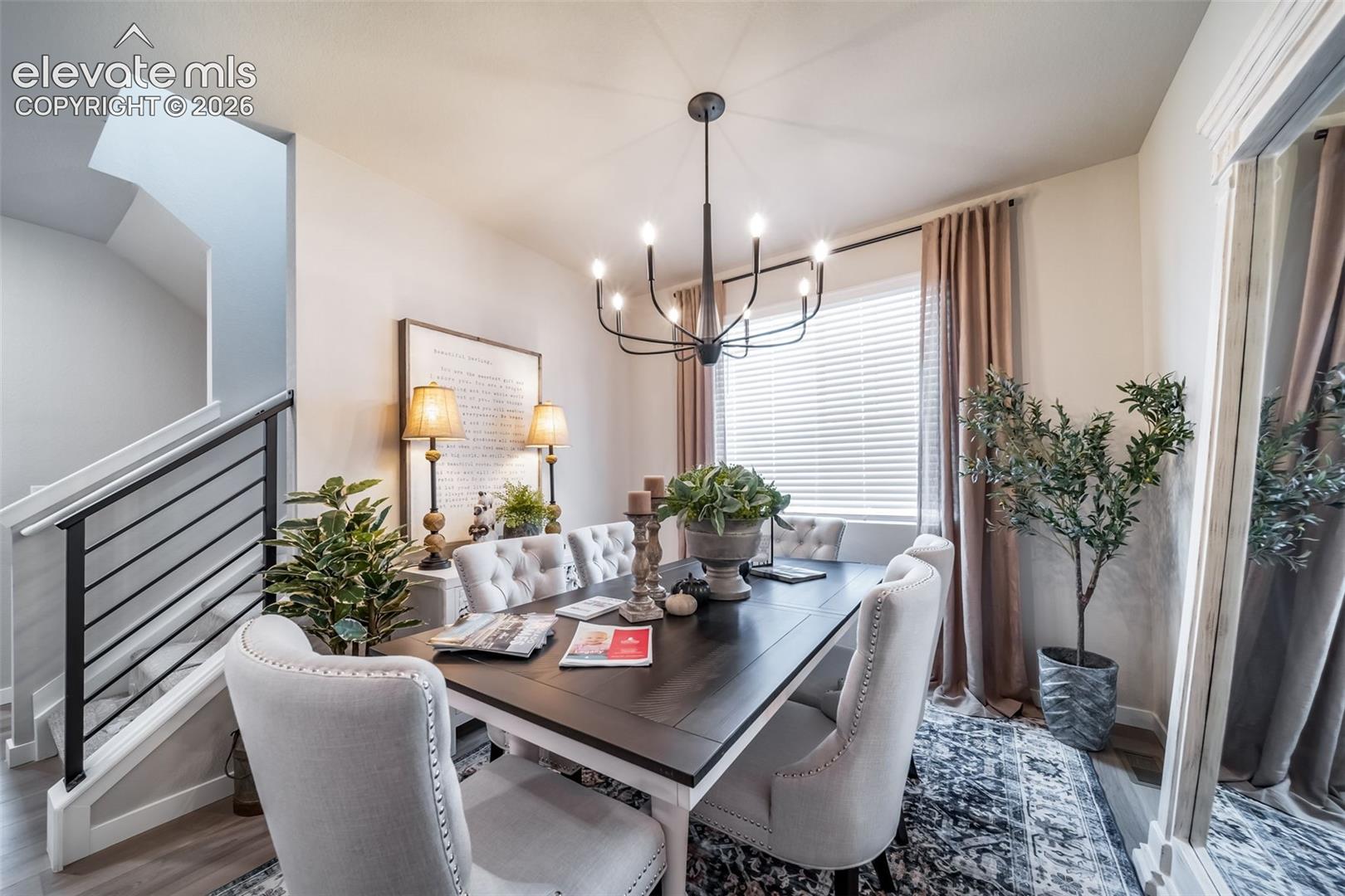 Dining area featuring a dark wood-finish table with light upholstered chairs, a contemporary chandelier, and a large window with blinds and drapes
*Photos of a model home*
