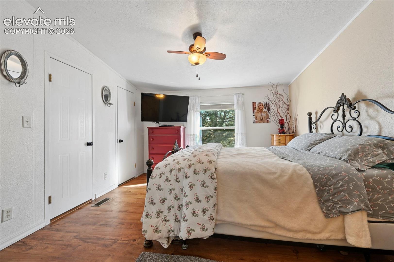 Room featuring wood-finish flooring, a ceiling-mounted light fixture with fan, and two white panel doors