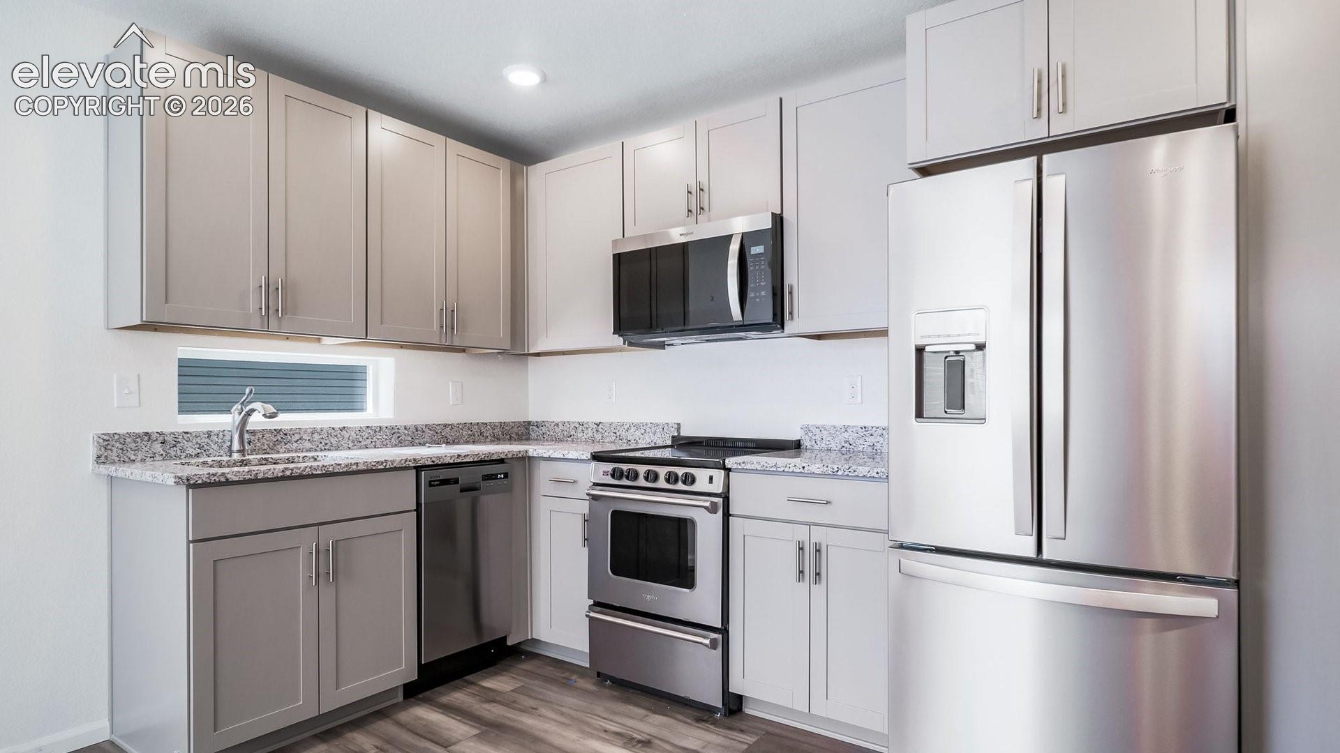 Kitchen featuring shaker-style cabinetry, stone-surface countertops, stainless steel appliances, and wood-finish flooring
*photos of a model home*