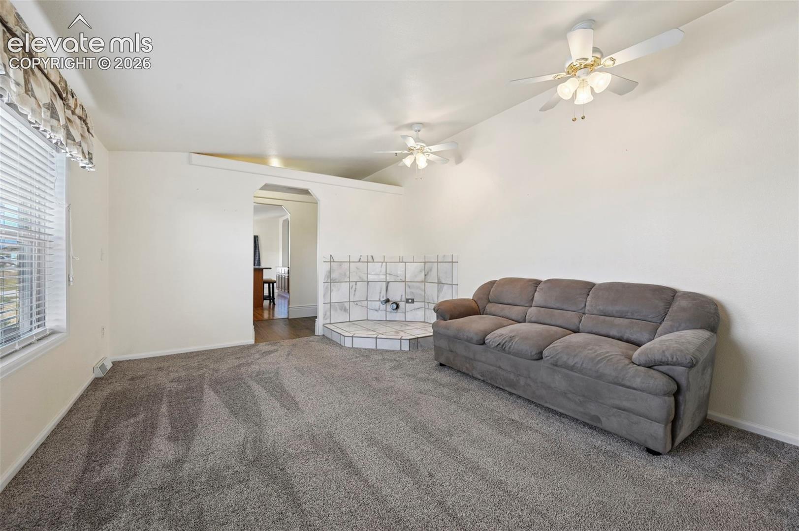 Living space featuring neutral carpeting, dual ceiling fans, and a tiled corner hearth