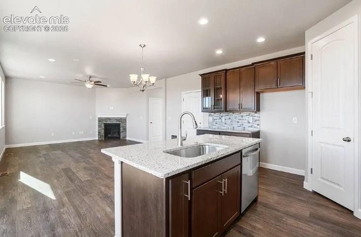 Kitchen featuring wood-finish cabinetry, stone-surface countertops, stainless steel undermount sink, and mosaic tile backsplash, accompanied by a stone-surround fireplace
