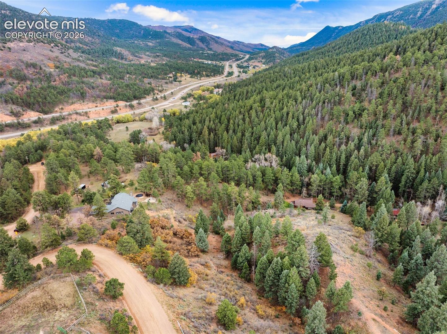 Aerial perspective of mountainous terrain featuring dense evergreen forest, winding gravel access roads, and natural ridgeline scenery