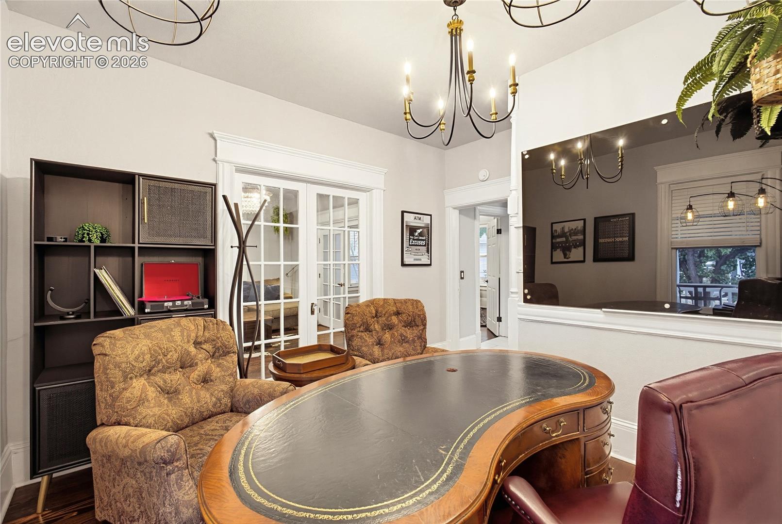 Room featuring a built-in shelving unit, double French doors, wood-finish flooring, a wall-mounted glass panel, and a multi-arm chandelier
