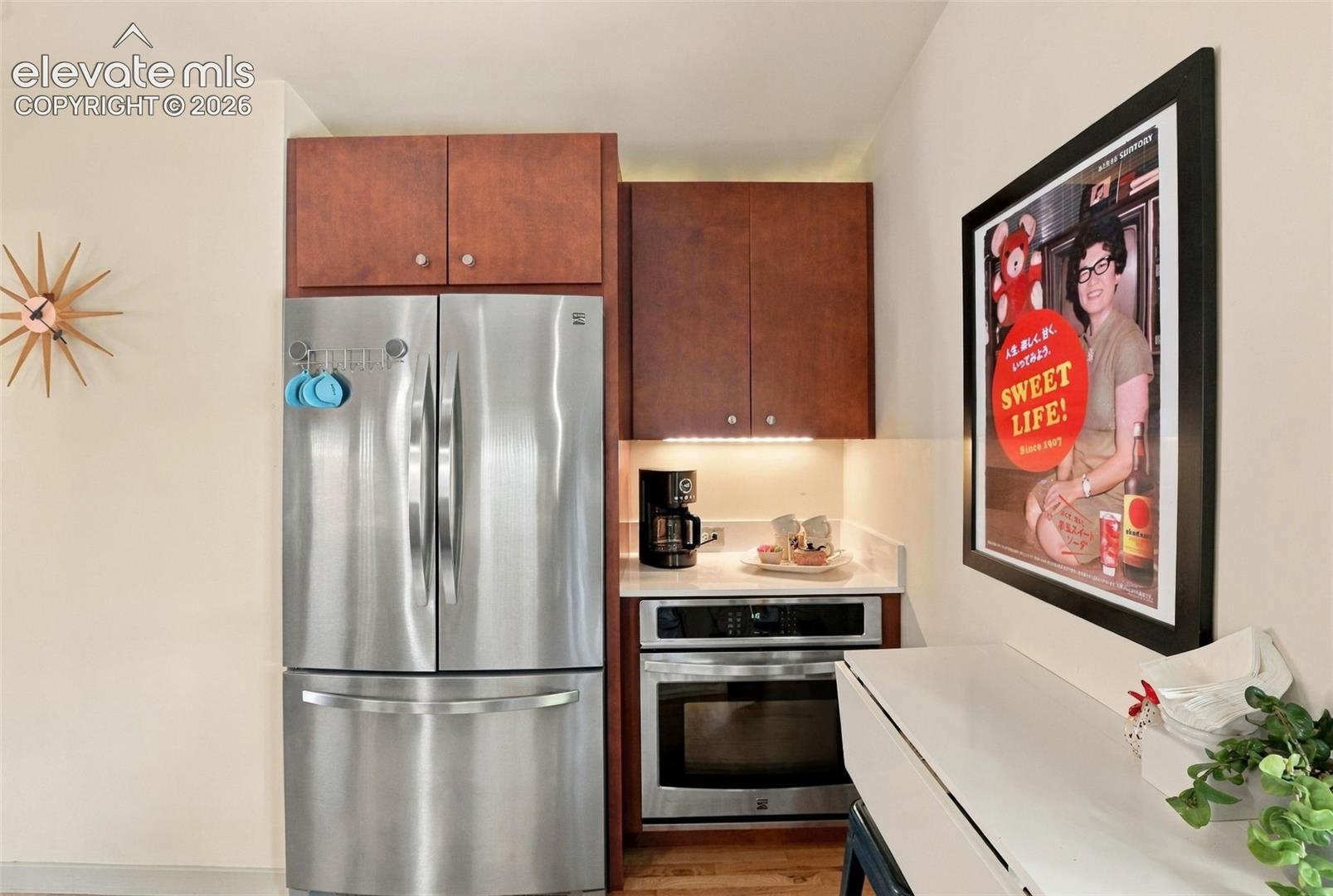 Kitchen featuring stained wood cabinetry, stainless steel French-door refrigerator, built-in stainless steel oven, and solid-surface countertop with under-cabinet task lighting