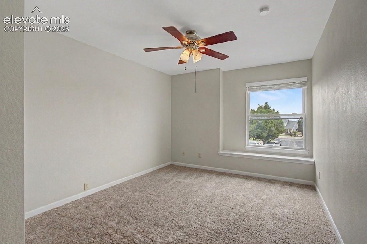 Carpeted room featuring a ceiling fan with light fixture, a window with blinds, and white baseboards