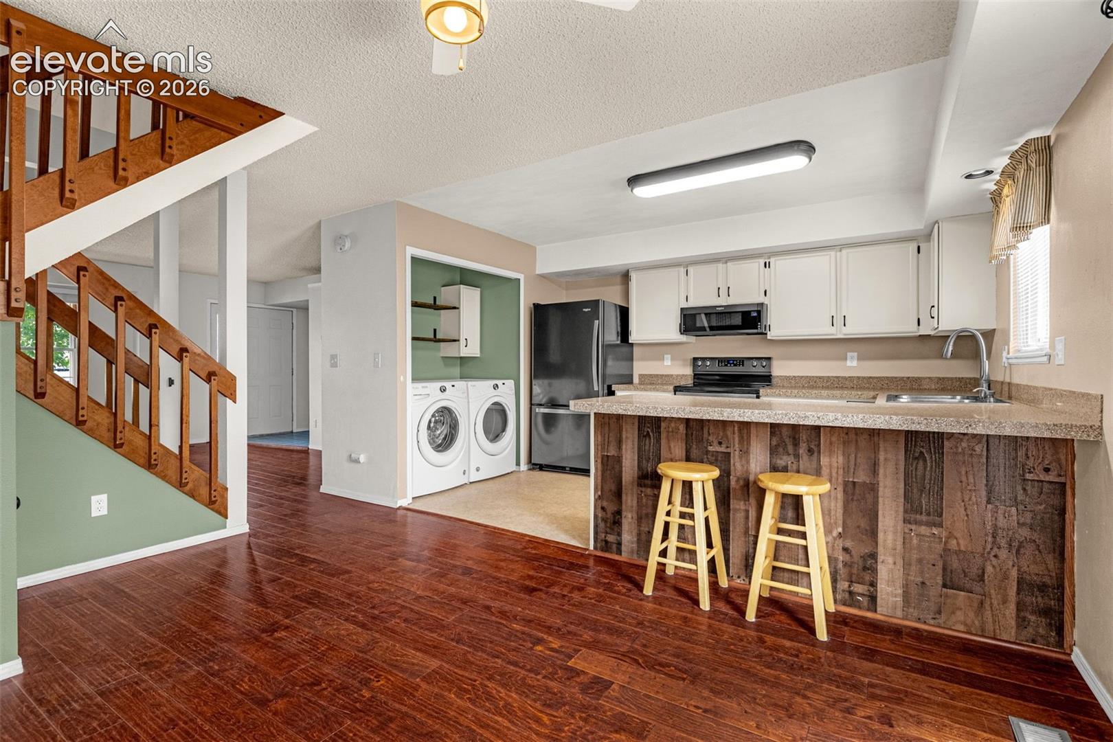Wood-finish flooring throughout, wood staircase, kitchen featuring white cabinetry, solid surface countertops, and an integrated laundry area