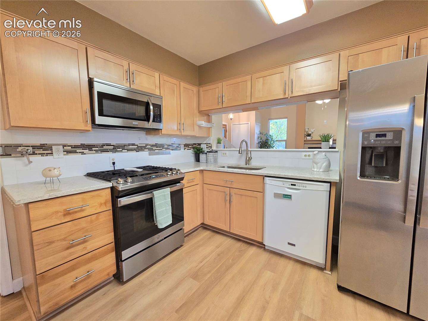 Kitchen featuring light-finish cabinetry, stainless steel appliances, a gas range, a multi-tonal tile backsplash, and light wood-finish flooring