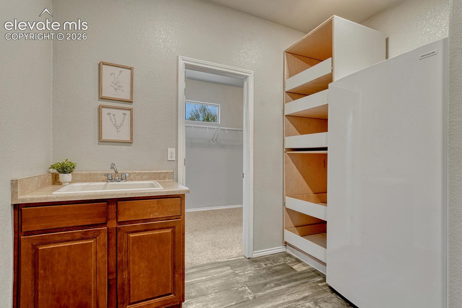 The main level Laundry Room features wood look tile flooring, a utility sink, built-in storage with pull-out shelves and a freezer that stays.