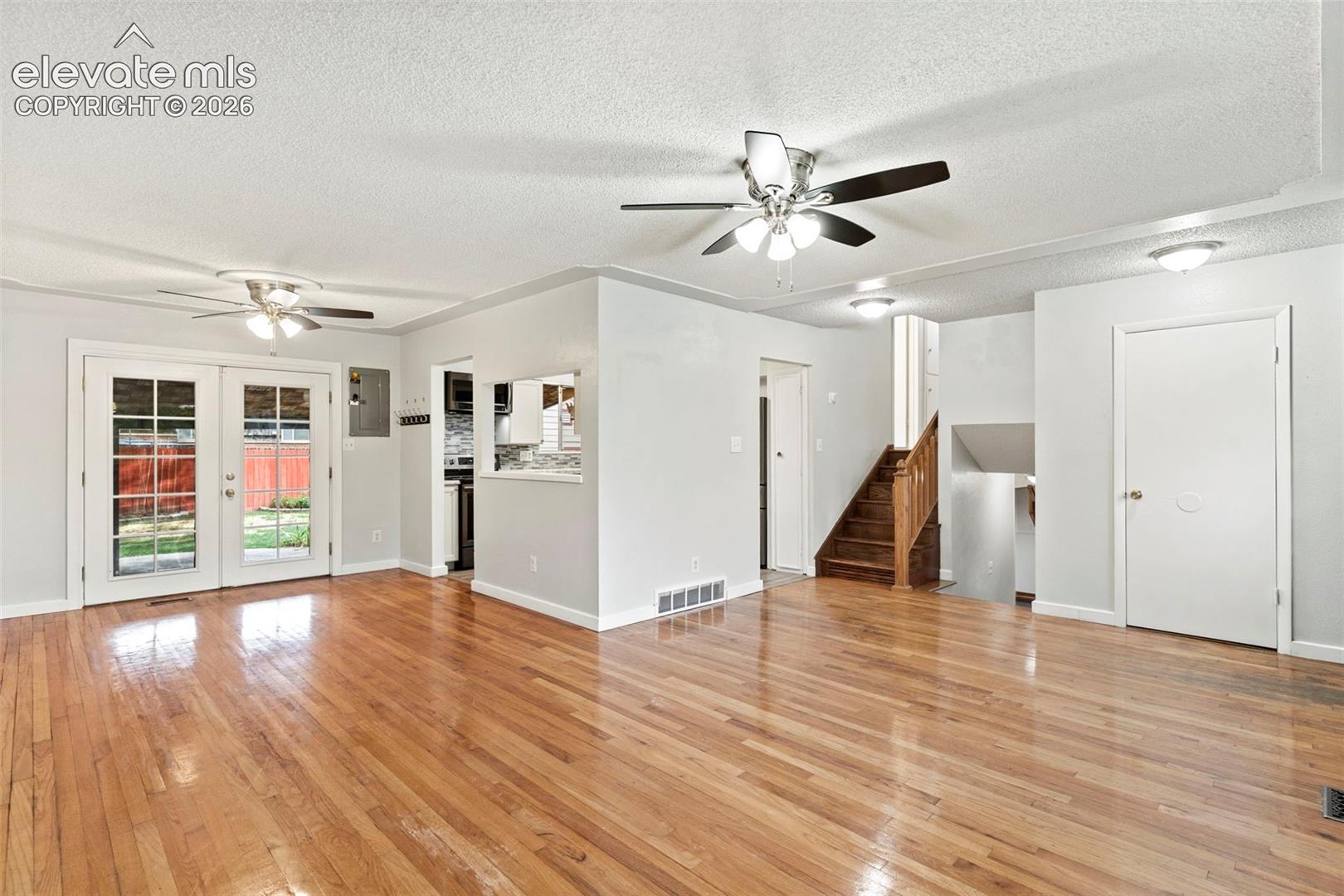 Hardwood flooring, white painted walls, French doors, ceiling fans, and a visible staircase