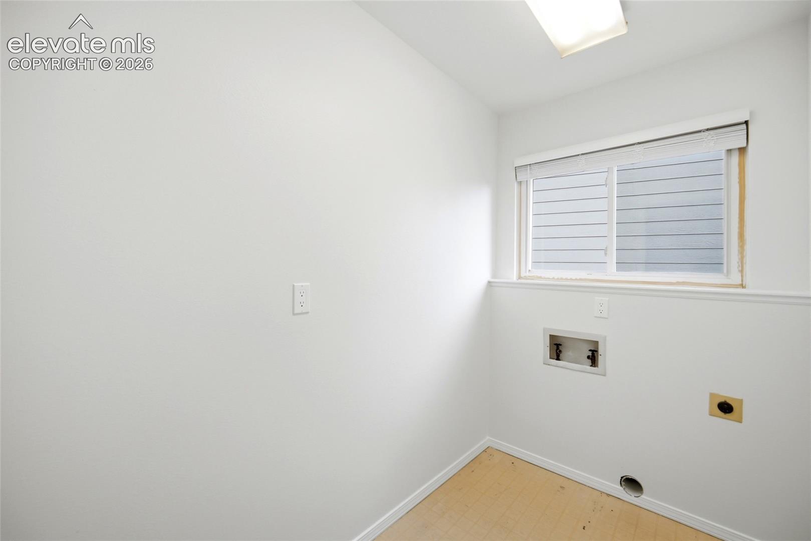 Utility space featuring a horizontal sliding window, neutral wall paint, overhead flush-mount lighting, and designated plumbing and electrical hookups