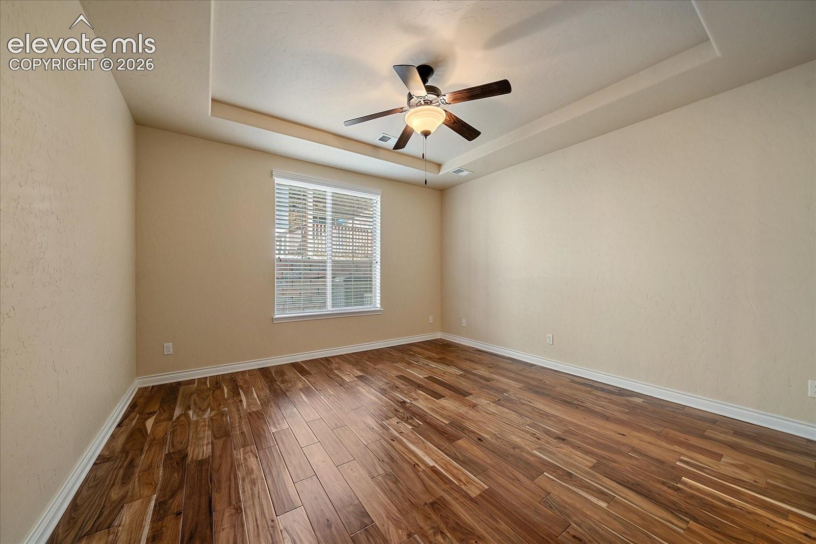 Tray ceiling featuring a central ceiling fan with integrated light fixture and wood-finish flooring