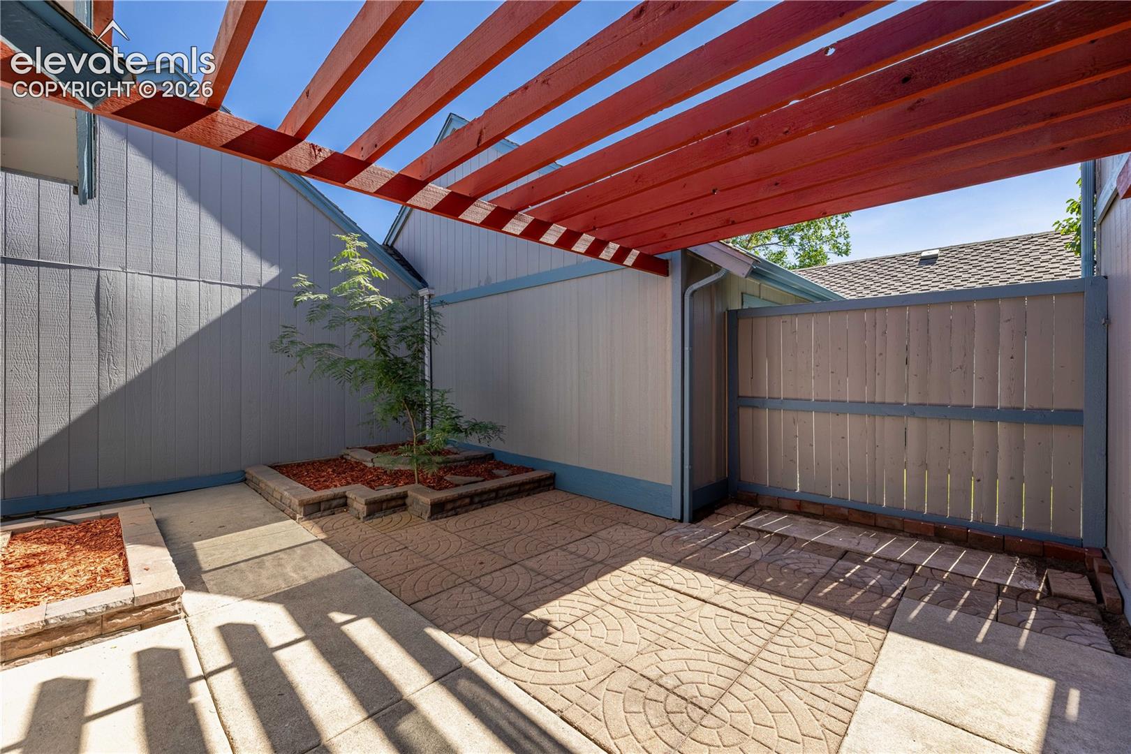 Private courtyard featuring a wood-beam pergola, patterned concrete pavers, and raised stone garden beds