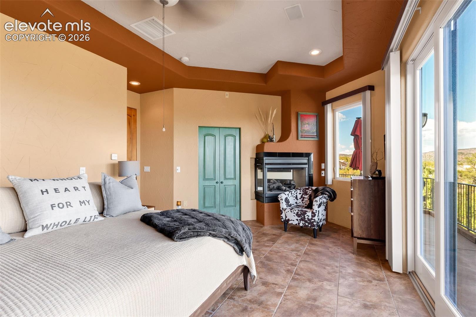 Interior space featuring a corner fireplace with a black surround, coffered ceiling, tile flooring, and glass sliding doors leading to an exterior balcony