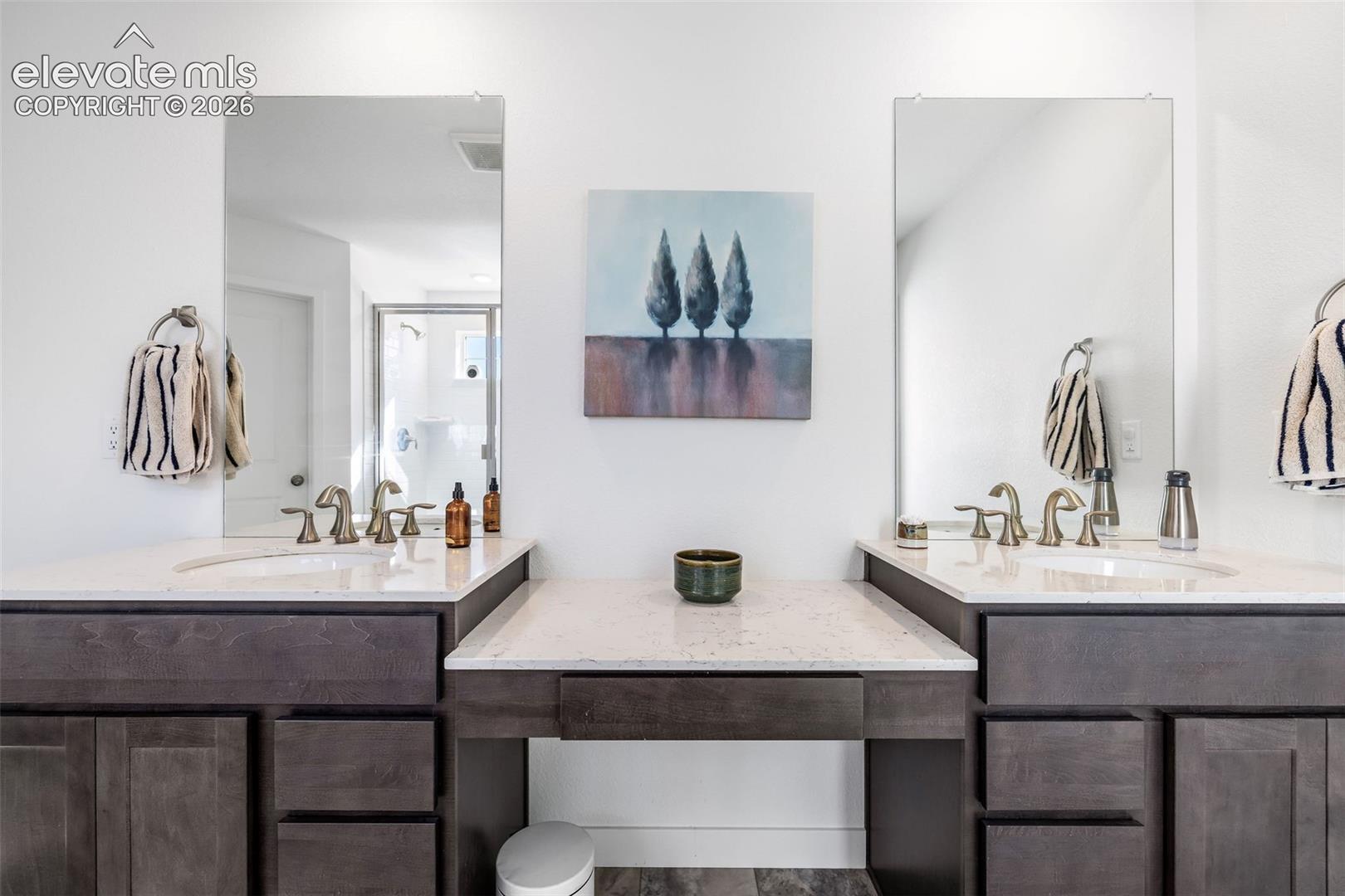 Dual vanity with white countertops, undermount sinks, bronze-finish faucets, and dark wood-finish cabinetry