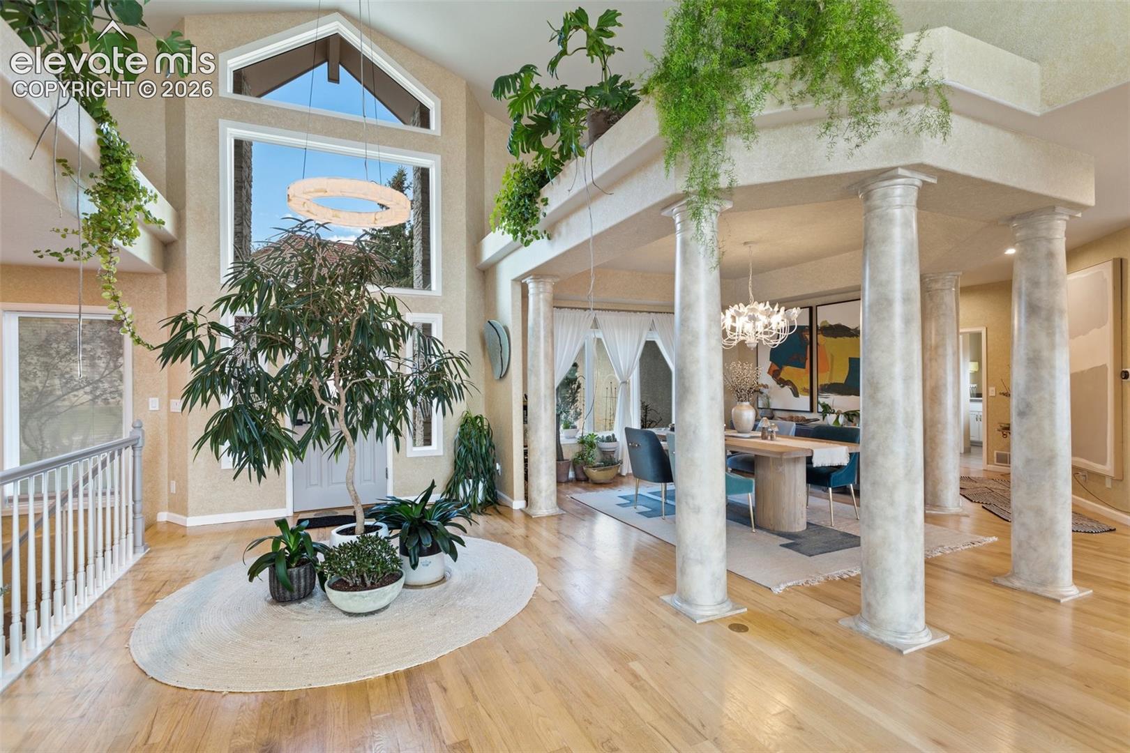 Grand entry foyer featuring light wood-finish flooring, a soaring vaulted ceiling, and a large arched window with a circular pendant light fixture