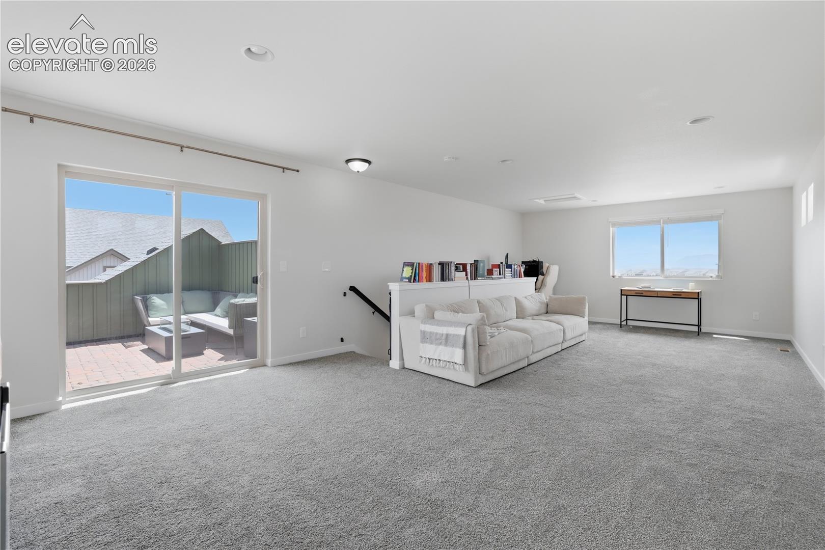 Spacious loft area featuring light gray carpeting, recessed lighting, and a large sliding glass door leading to an outdoor patio with brick-style pavers