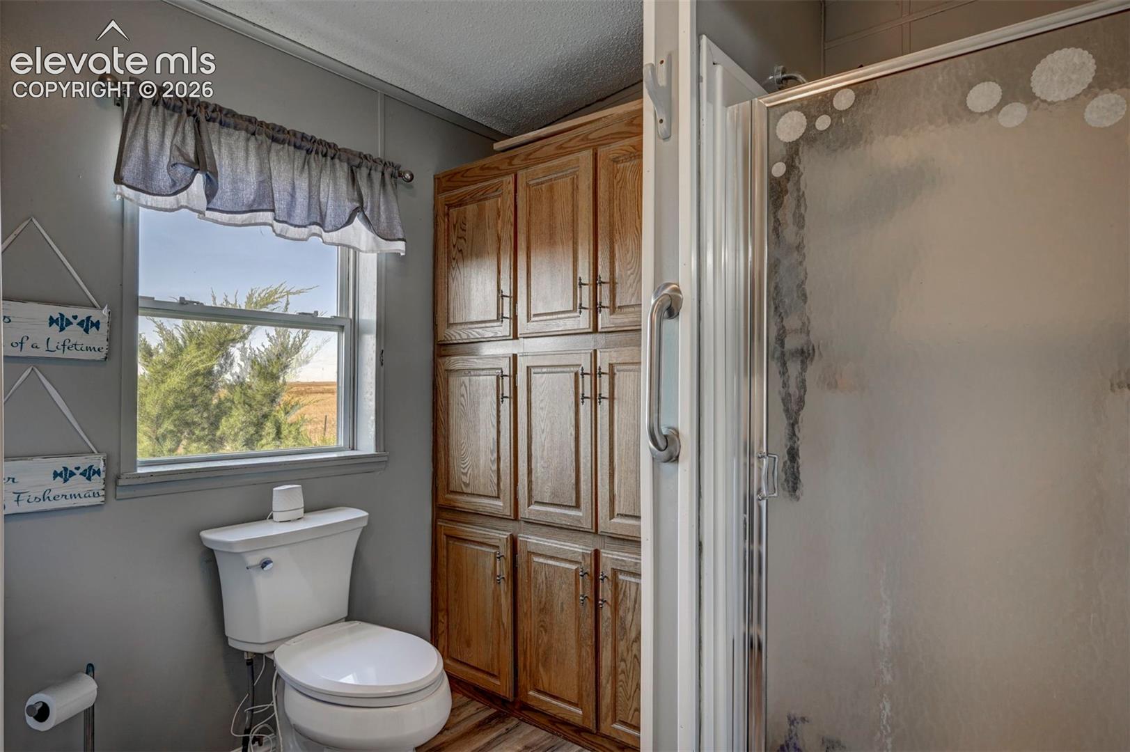 Full bath featuring a textured ceiling, a shower stall, and wood finished floors