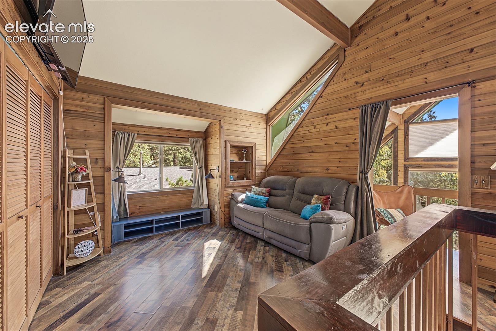 Wood-paneled interior with exposed wood beams, wood-finish flooring, and multiple windows