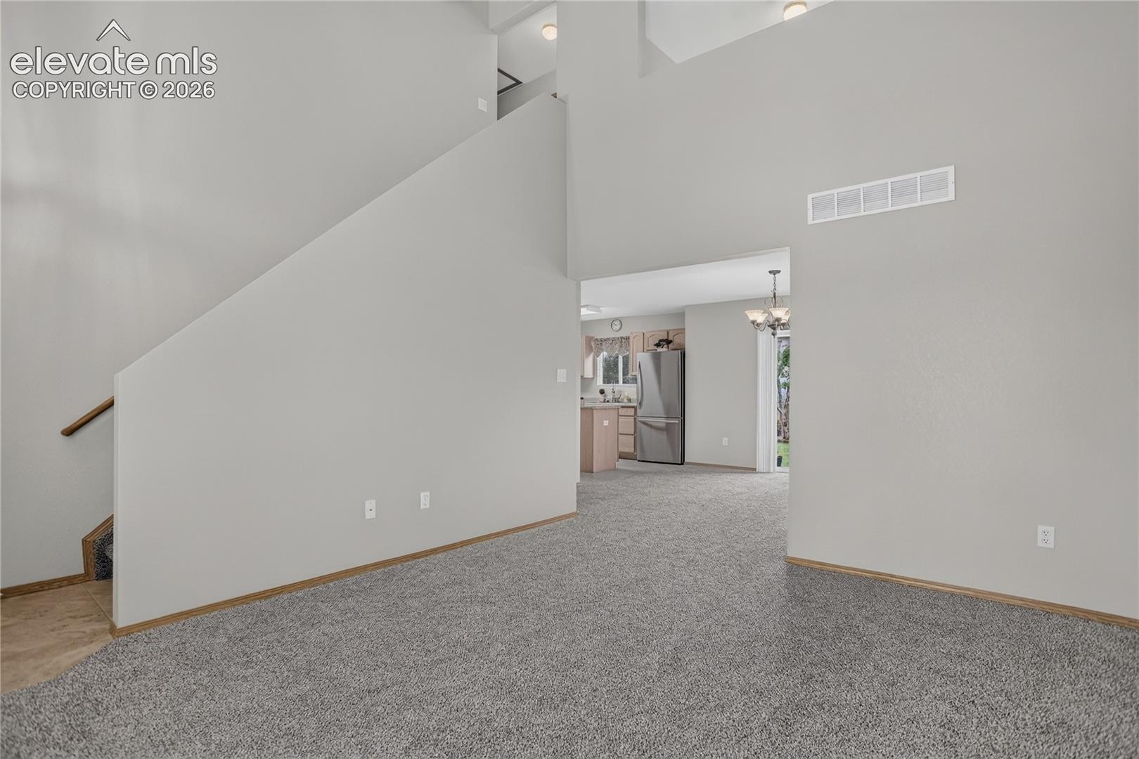 Vaulted ceiling with recessed lighting, light gray wall finishes, gray carpeting, and a wood-finish stair railing