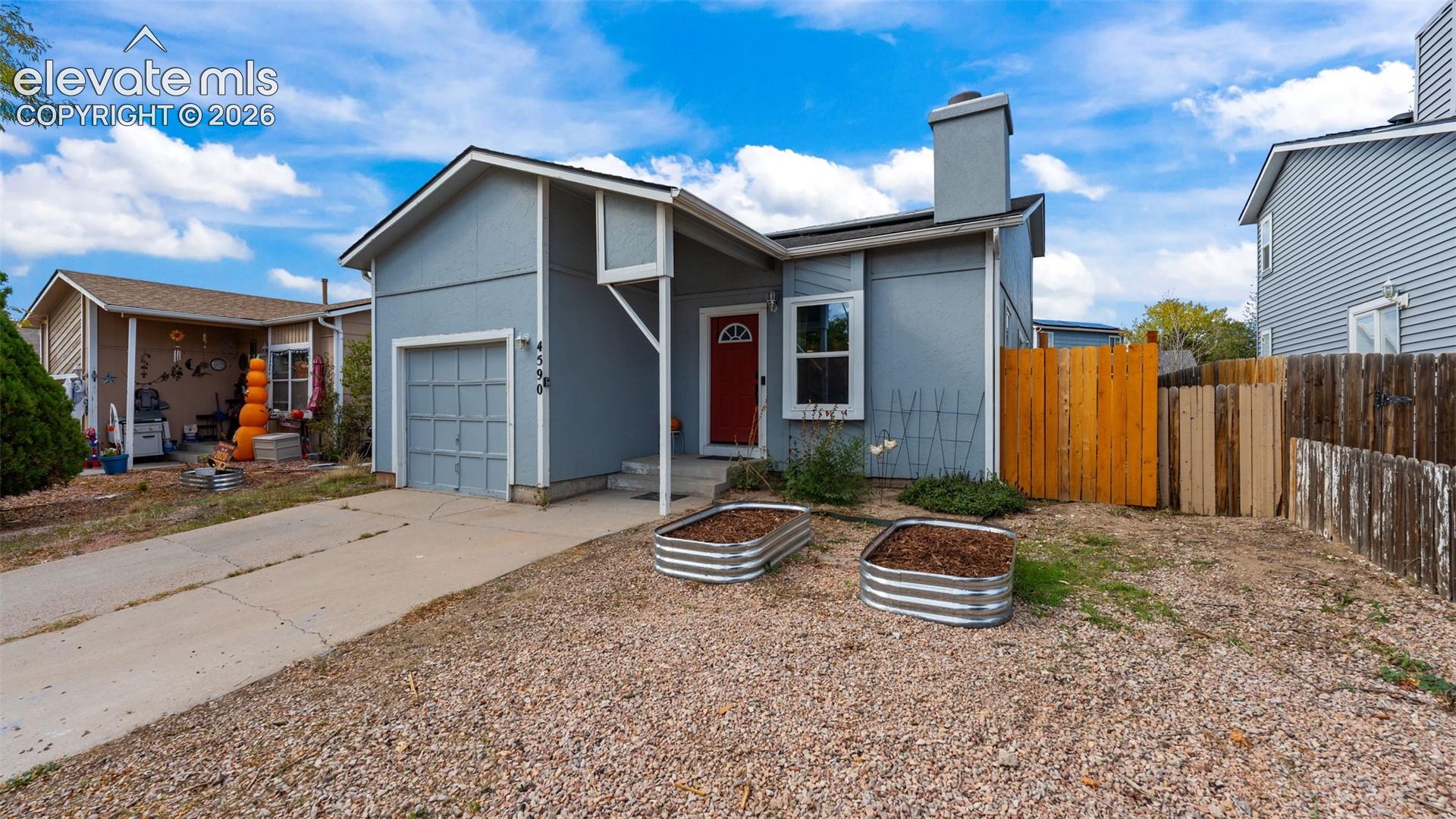 Exterior featuring a painted finish, attached single-car garage, prominent chimney, wood-style privacy fencing, and two metal raised garden beds