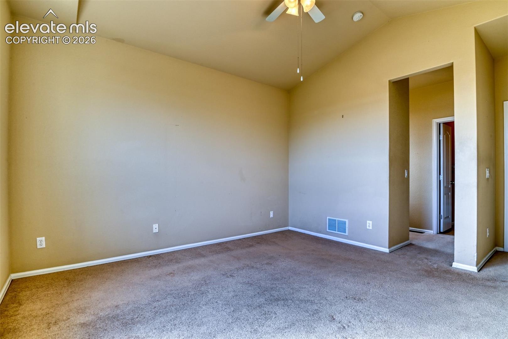 Vaulted ceilings featuring a central ceiling fan, neutral wall finishes, and carpeting