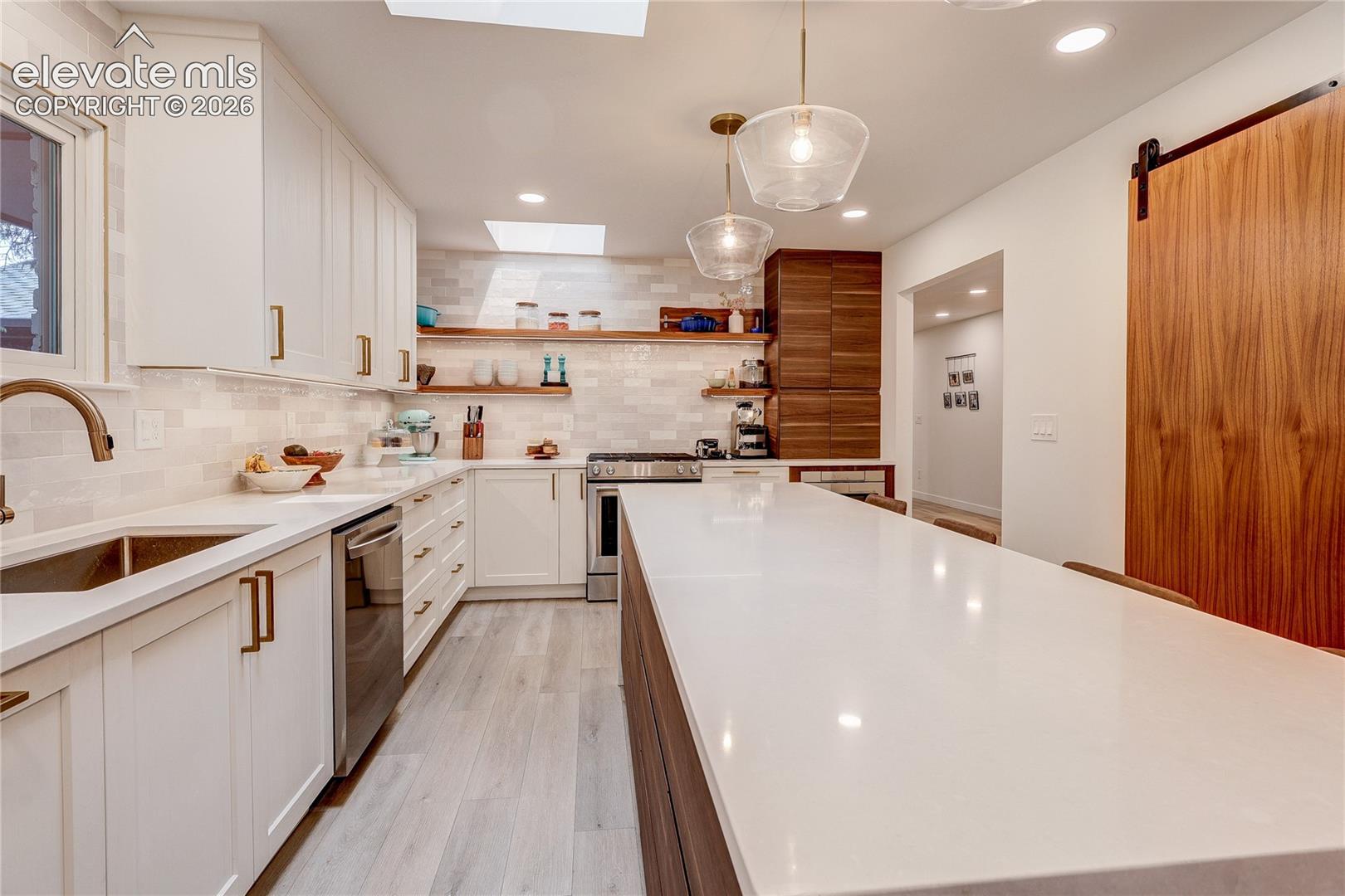 Modern kitchen featuring white cabinetry, a large center island with a light-toned countertop, wood-finish flooring, and a barn door