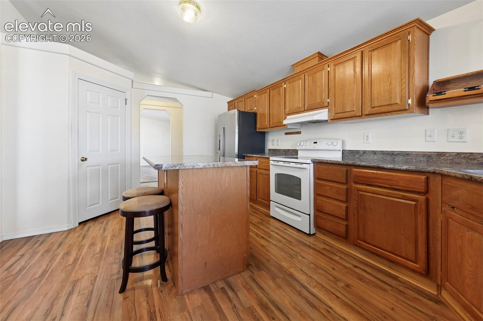 Kitchen featuring wood cabinetry, an island with stone-surface countertop, stainless steel refrigerator, and wood-finish flooring