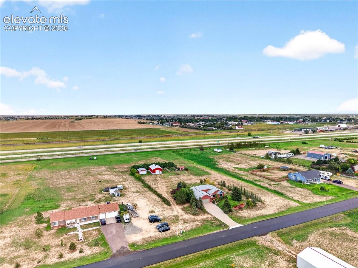Aerial perspective of a sprawling rural property featuring a multi-car garage, multiple accessory structures, expansive acreage, and paved road frontage