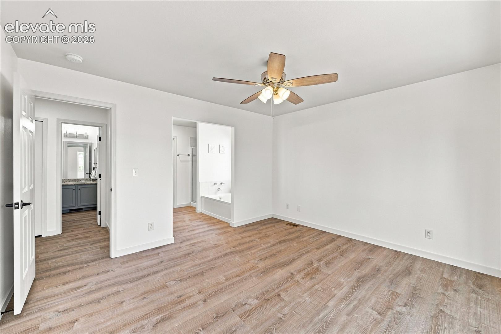 Light wood-finish flooring, ceiling fan with integrated lighting, recessed tub, and gray vanity with countertop and mirror