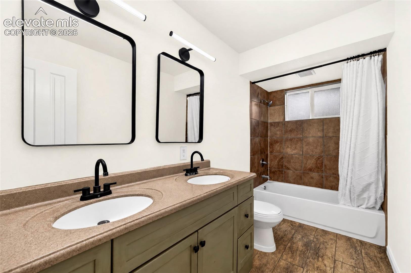 Dual-sink vanity with matte black fixtures, quartz-finish countertop, framed wall-mounted mirrors, and tiled tub-shower enclosure