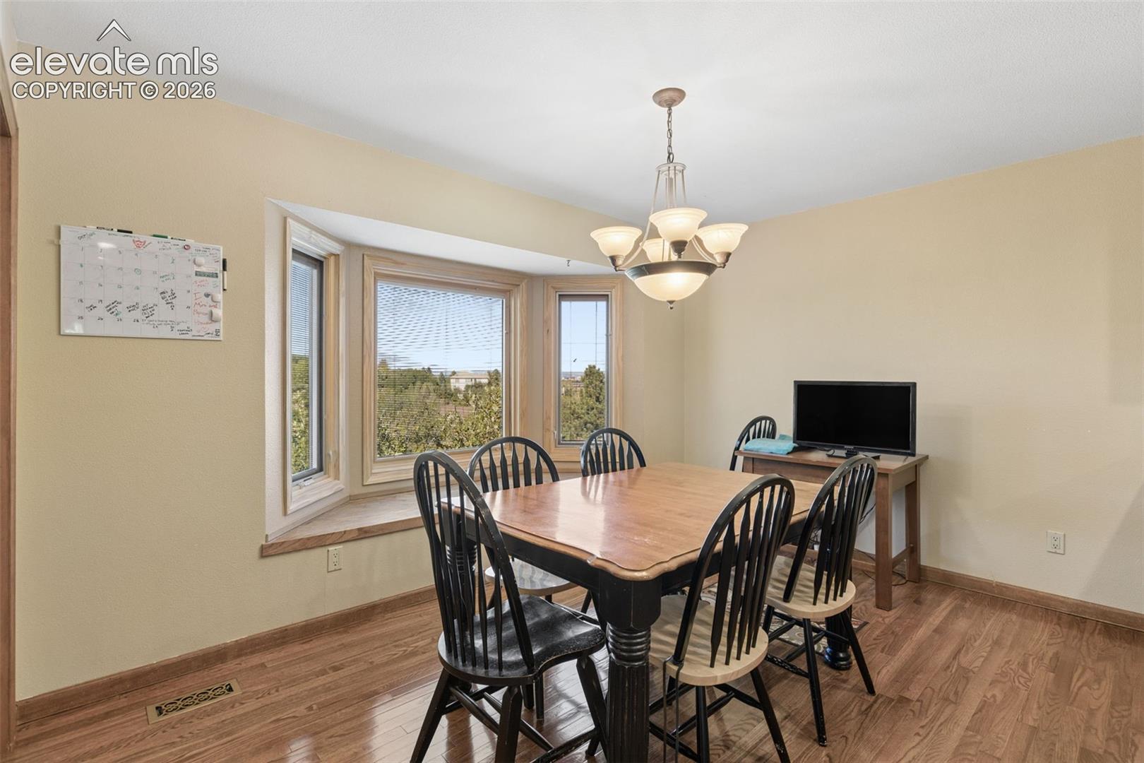 Bay window with a built-in seat, wood-finish flooring, and a multi-arm pendant light fixture