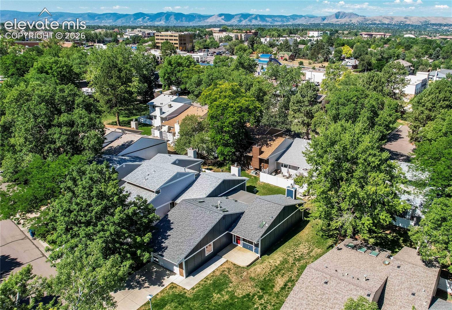 Aerial perspective of property featuring an asphalt shingle roof, concrete driveway, attached garage, and mature tree canopy, set against a backdrop of mountain terrain