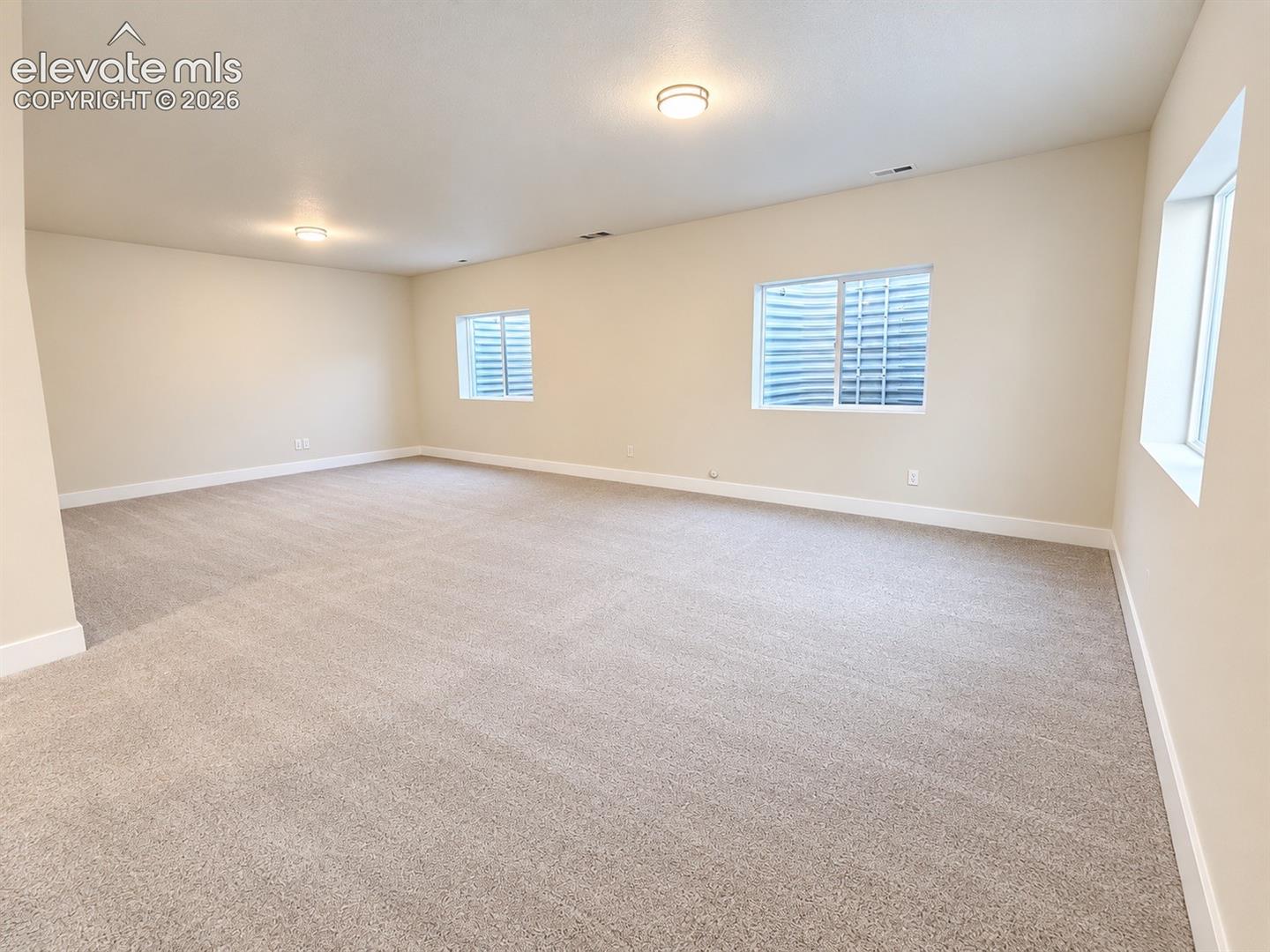 Expansive room featuring neutral-toned carpeting, light beige walls, and multiple recessed windows