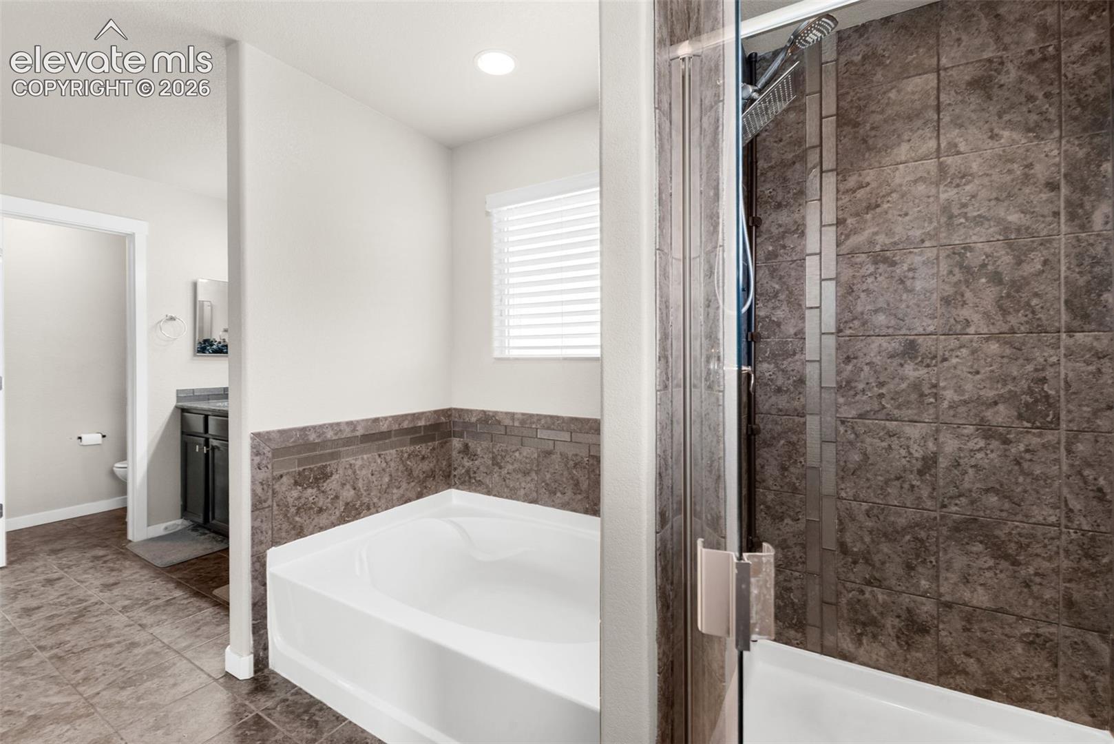 Bathroom featuring a glass-enclosed shower with tile surround, a deep soaking tub with a tiled splash, and tile flooring