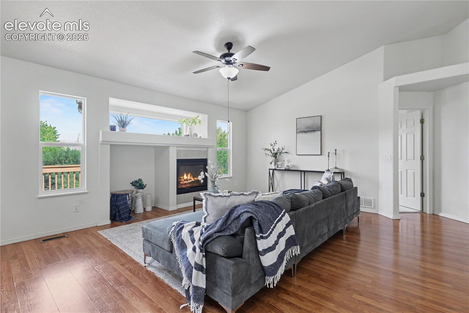 Living area with wood-finish flooring, vaulted ceilings, and a fireplace featuring a tile surround