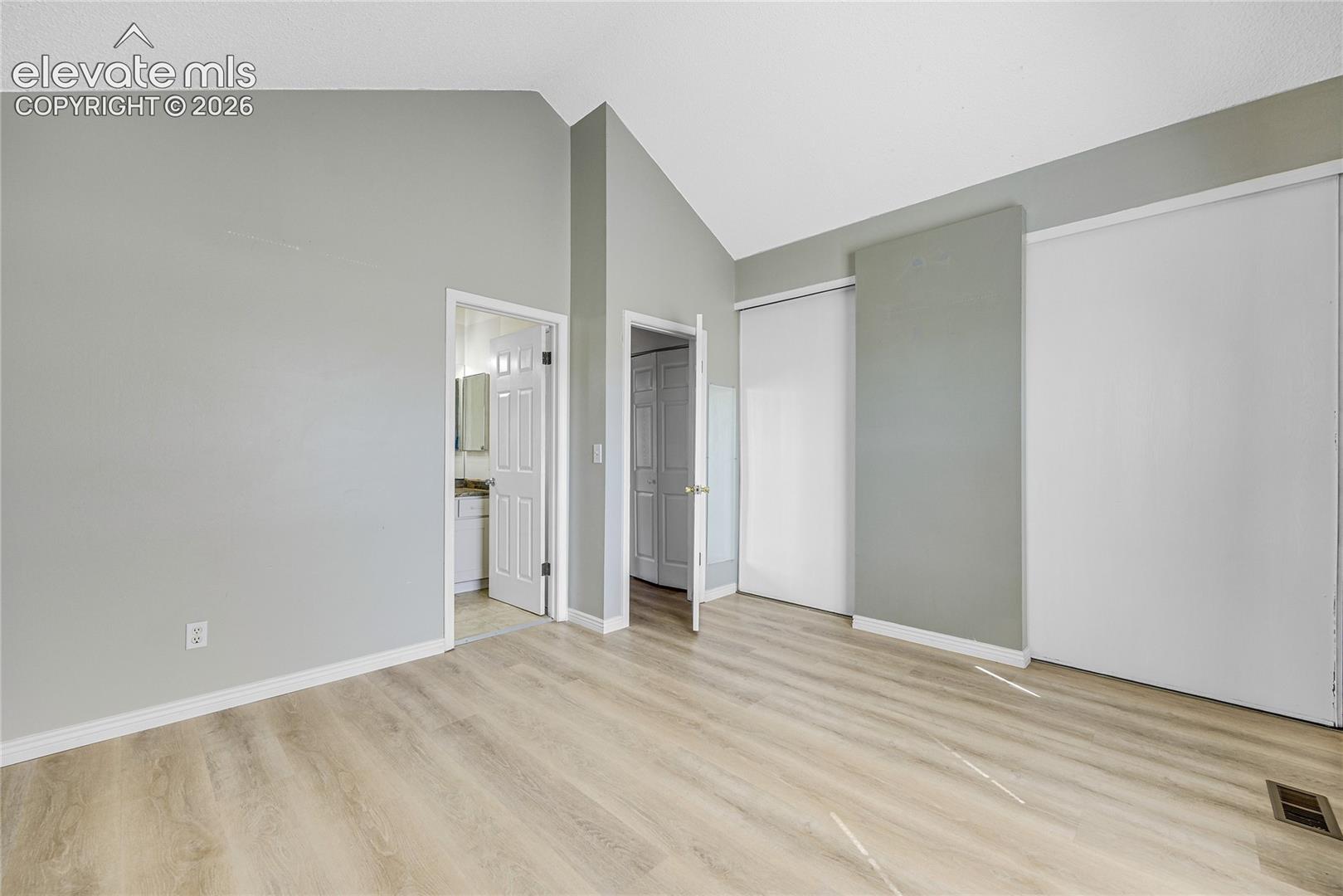 Vaulted ceiling with light gray walls, wood-finish flooring, and white trim